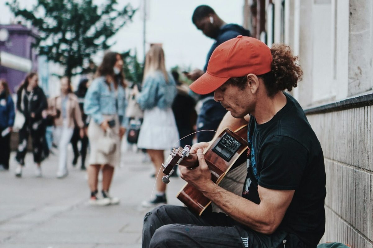 person playing guitar in park with tip jar and smiling crowd.jpg